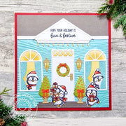 Handmade holiday card featuring a turquoise house with a white front door, penguins, Christmas trees, a wreath, & lanterns.