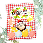 A handmade Christmas card featuring a red & white gingham background, a penguin in a Santa hat, and big colorful ornaments.