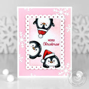 Handmade Christmas card featuring peeking penguins wearing Santa hats on a pink snowflake background with a scalloped frame.