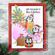 Holiday Christmas card scene: penguins wearing Santa hats sit in a pink sleigh with a decorated holiday tree and gifts.