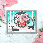 Christmas card featuring a holiday wreath with a big pink bow, surrounded by snowy birch trees and deer in the background.